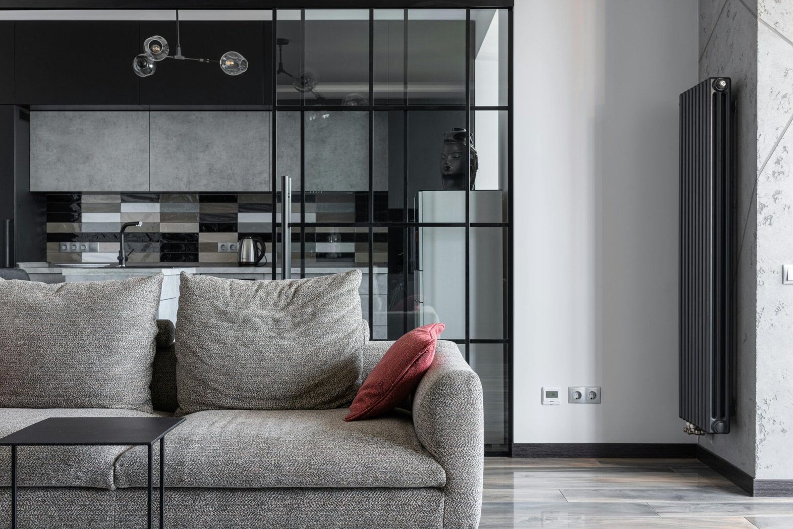 Contemporary living space featuring a stylish gray sofa, red cushion, and a view into a modern kitchen.