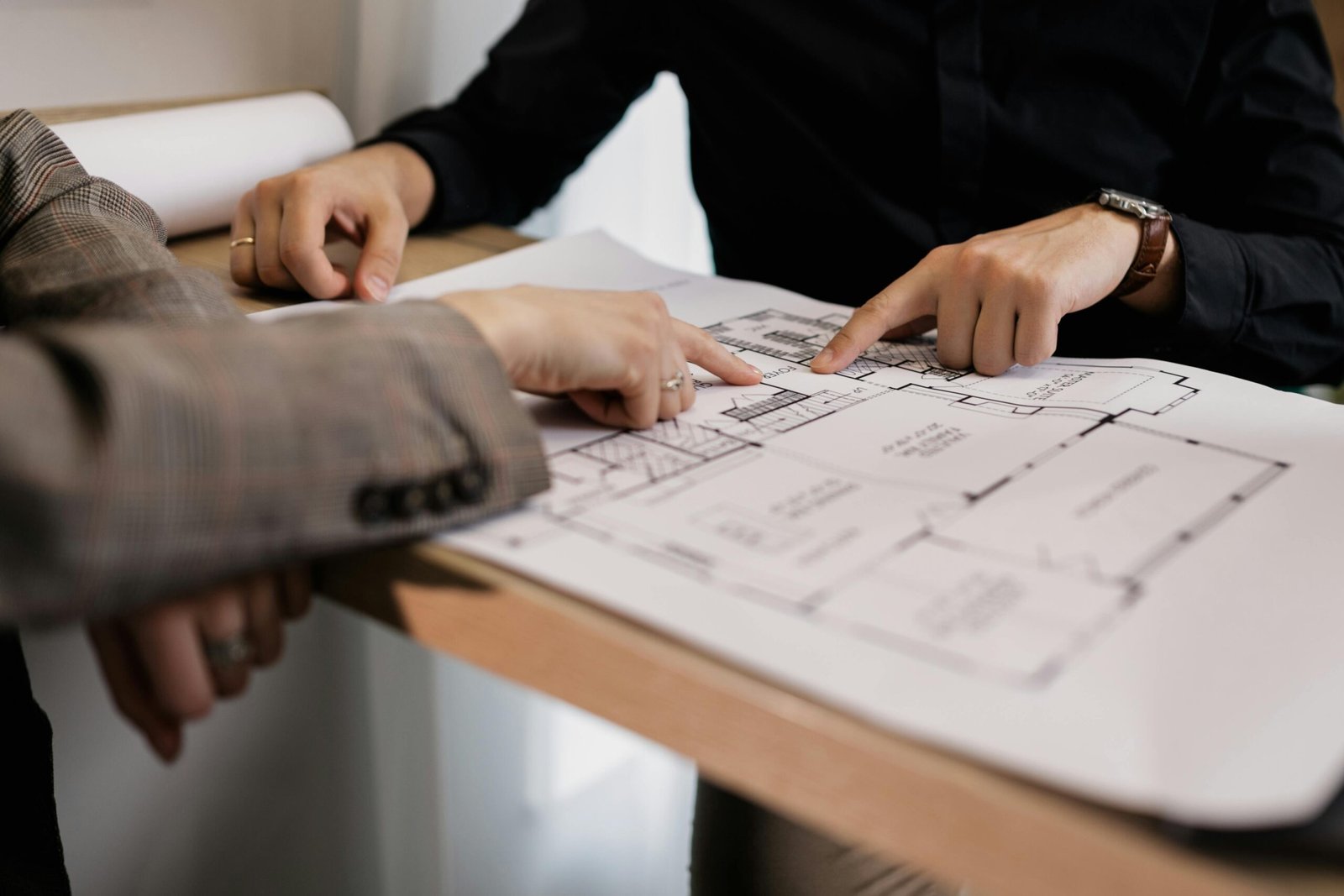 Two architects reviewing and pointing at a detailed floor plan on paper in an office setting.